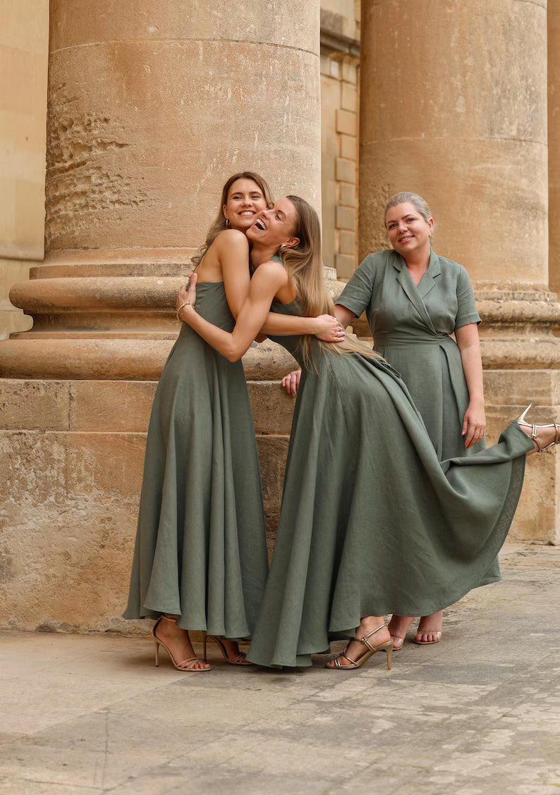 Zwei Frauen tragen lange olivgrüne Kleider aus fließendem Stoff vor klassischer Architektur